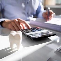 Chest down view of man using calculator at a desk next to a fake tooth