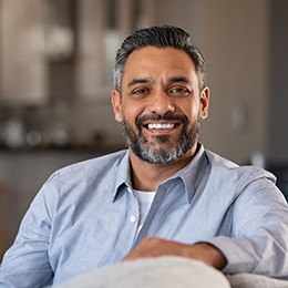 Man in blue shirt smiling while sitting on couch at home