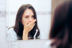 woman holding her mouth in front of a bathroom mirror